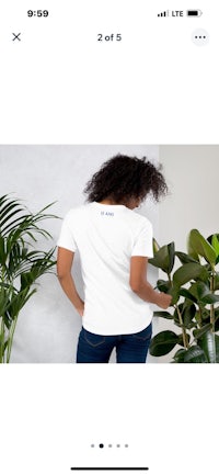 a woman is standing next to a plant in a white t - shirt